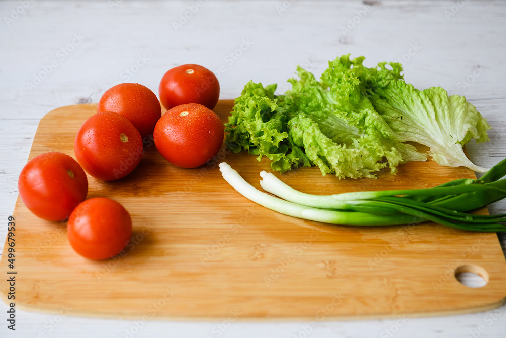 Fresh vegetables for salad lie on a wooden table with a cutting board. Fresh vegetables for salad lie on a wooden table with a cutting board.