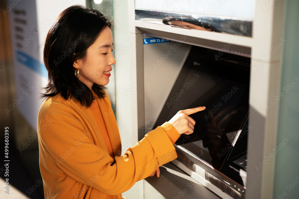 Happy smiling young woman withdrawing money from credit card. Young woman typing pin code on keypad of ATM machine Happy smiling young woman withdrawing money from credit card. Young woman typing pin code on keypad of ATM machine