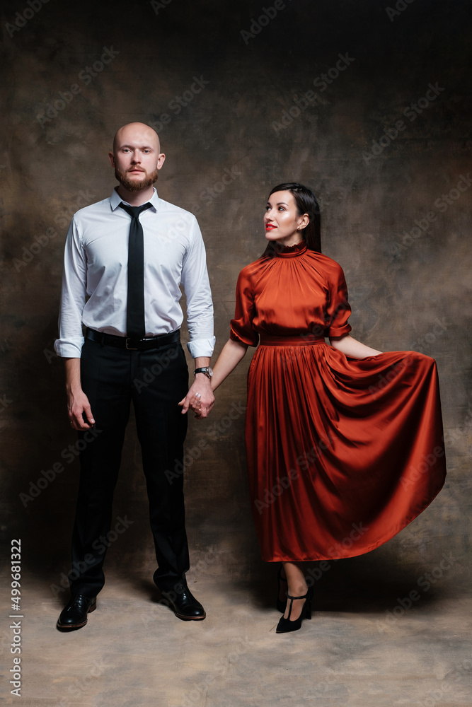 A girl in a red dress and bald bearded man. Lovely couple posing.