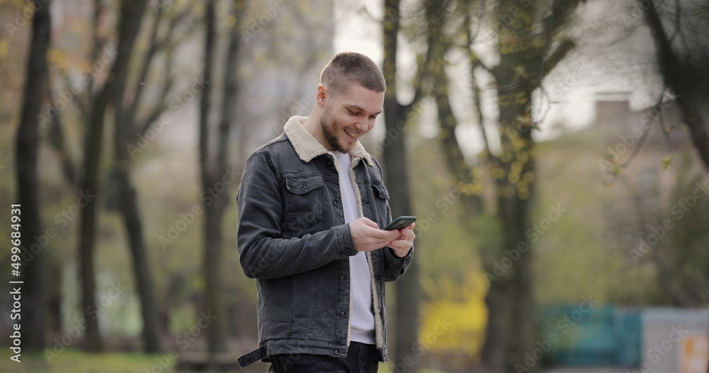 Smiling man use smartphone walking in the park Smiling man use smartphone walking in the park