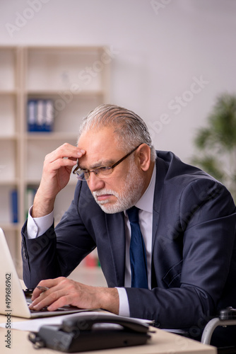 Old male employee in wheel-chair sitting at workplace