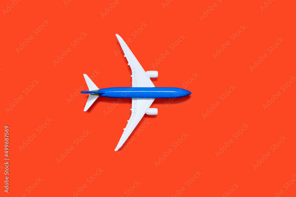 Model of a blue-white aircraft on an orange background. Tourism or freight transport concept. Top view toy airplane on orange background