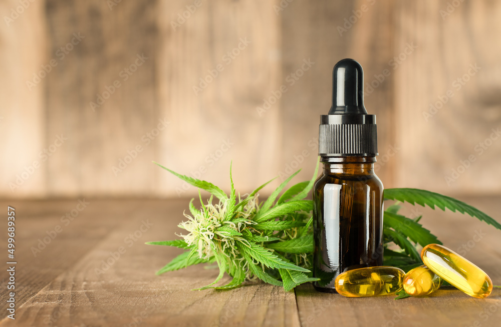 CBD oil, cannabis plant and capsules on wooden background CBD oil, cannabis plant and capsules on wooden background