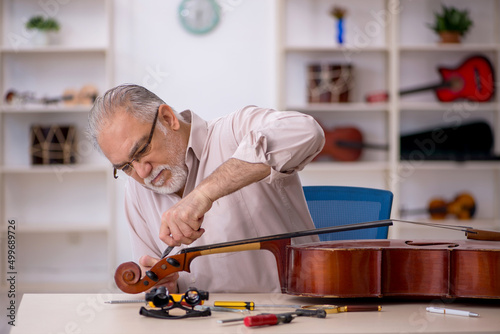 Fotografie Old male repairman repairing musical instruments at workshop