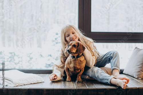 Little girl with her dog sitting by the windwo at home photo