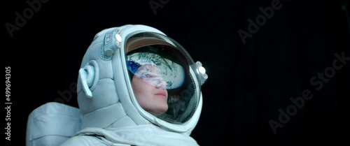 CU Portrait of Caucasian female astronaut during spacewalk. Earth reflecting in helmet visor. Space exploration concept. Shot with 2x anamorphic lens