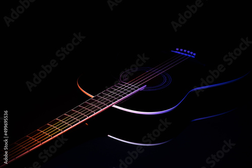 black guitar on a dark background under beam of colored light with copy space. guitar music low-key concept diagonal projection