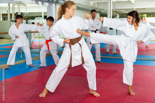 Two girls working in pair mastering new karate moves during group class with female coach