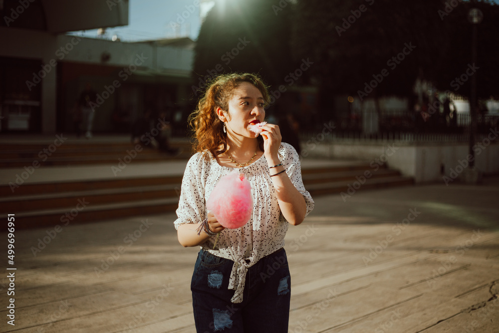 Fototapeta premium mujer degustando Algodón de Azúcar en un parque mientras esta de vacaciones.