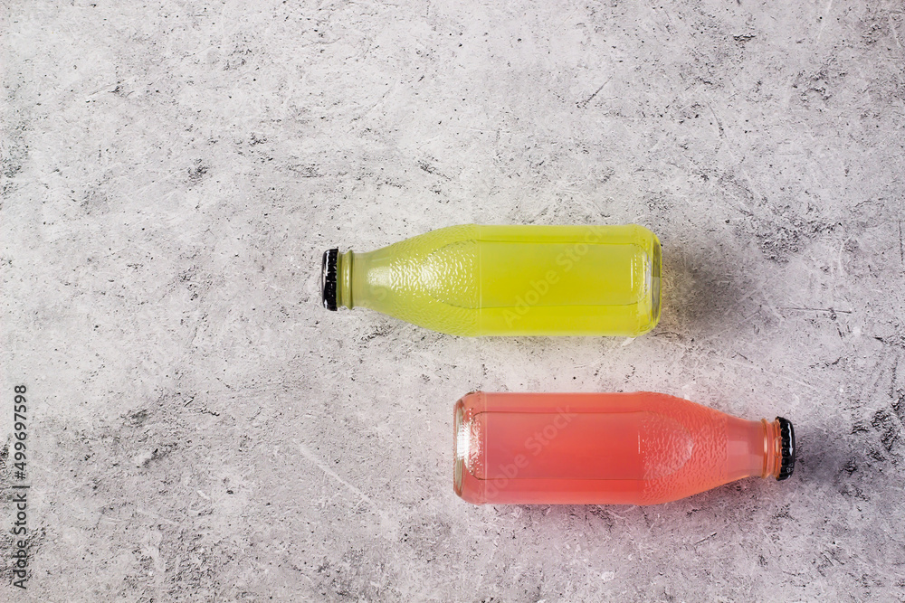 Two cylindrical bottles showcasing vibrant drinks in yellow and pink against a matte stone background. Two cylindrical bottles showcasing vibrant drinks in yellow and pink against a matte stone background.