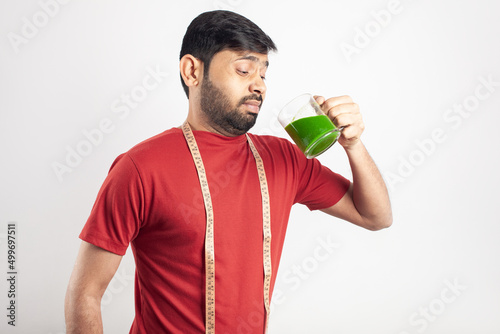 young asian man making negative face while drinking wheat grass juice or vegetable smoothie