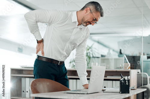 Ooo, my back is killing me. Shot of a mature businessman standing alone in his office and suffering from backache.