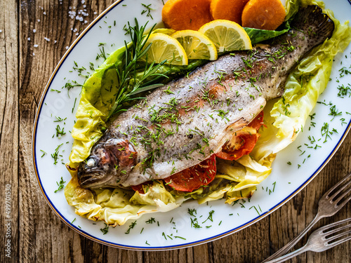 Roast trout with potatoes and tomatoes on green cabbage leaves served on wooden table
