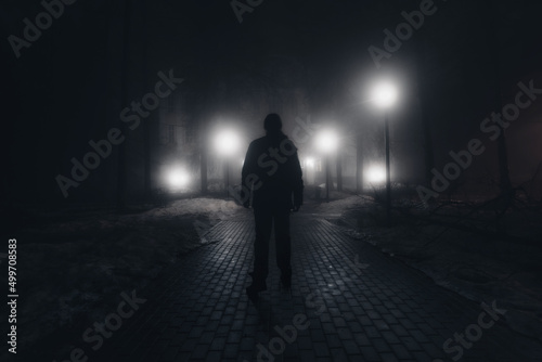 Sad man alone walking along the alley in night foggy park