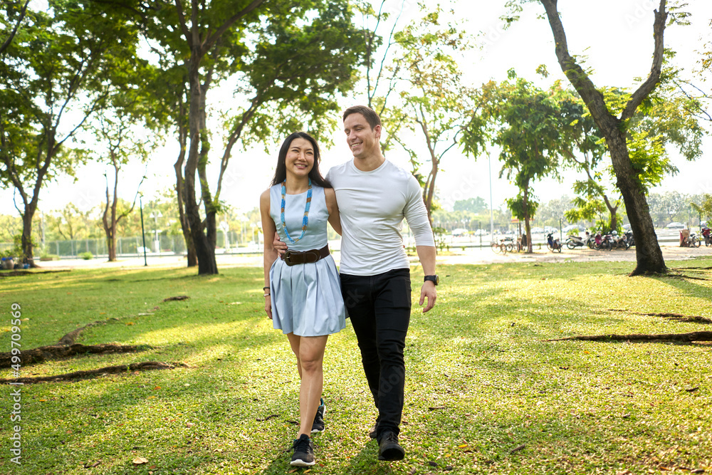Multiracial couple walking in a park holding each other's backs