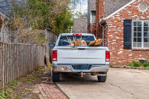 White pickup truck full of trash-boards and boxes- parked in driveway of brick house by security fence - ready to haul it away photo