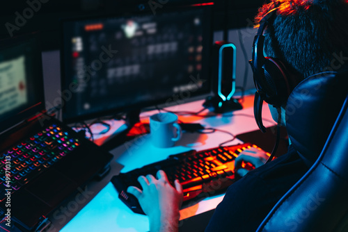 Young man addicted to video games playing on a computer with headphones. Young gamer illuminated with coloured lights