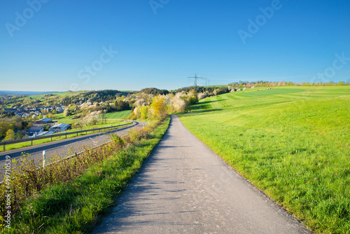 Path in the countryside between a agricultural field and a road, landscape in Germany, blue sky in the spring