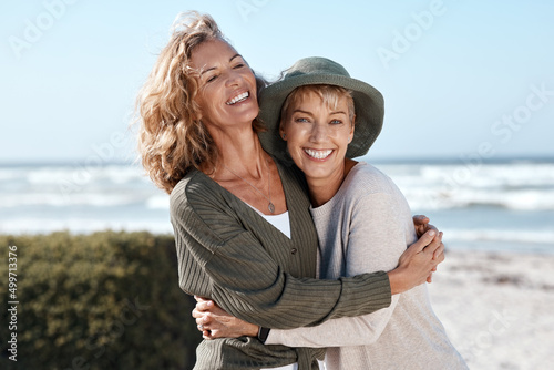 Best friends for life. Cropped shot of two attractive mature women hugging while standing on the beach. photo