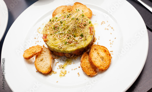 Gourmet salmon tartare with guacamole and toasted bread served on white plate
