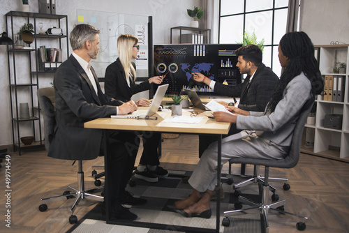 Pretty concentrated blond female and serious indian businessman manager at a meeting together with their diverse multiracial colleagues, in modern boardroom with big TV plasma screen presenting charts