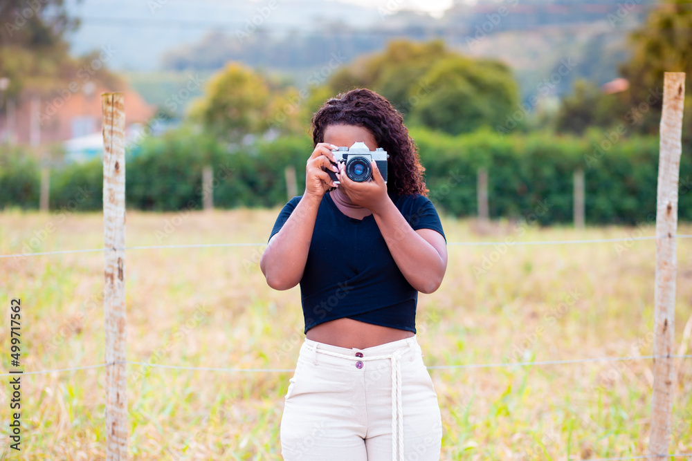 Young black woman holding a retro photo camera and taking pictures of rural landscape. Concept of creativity and artistic production.