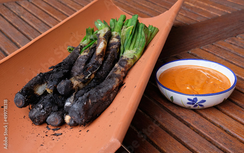 Calçots served in a tile. Typical food from Catalonia, Spain, which is usually served in a tile with a bowl of sauce similar to romesco. photo