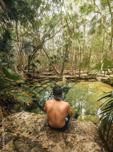 young hispanic man with hat enjoy looking at a cenote in mexico