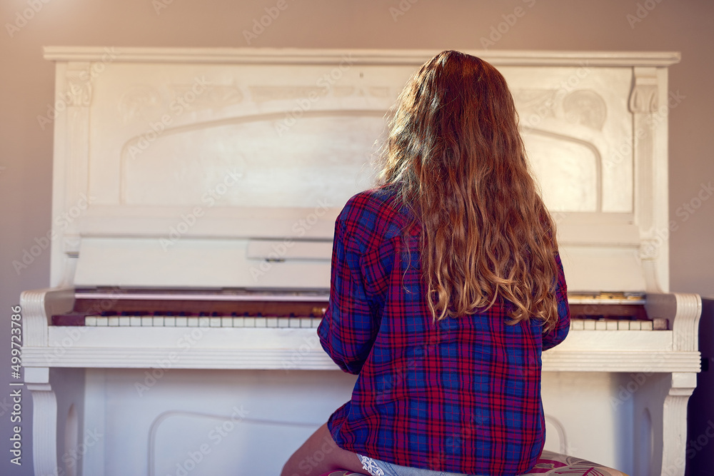Practising her piano lesson. Rear view shot of a young girl playing the piano. Practising her piano lesson. Rear view shot of a young girl playing the piano.