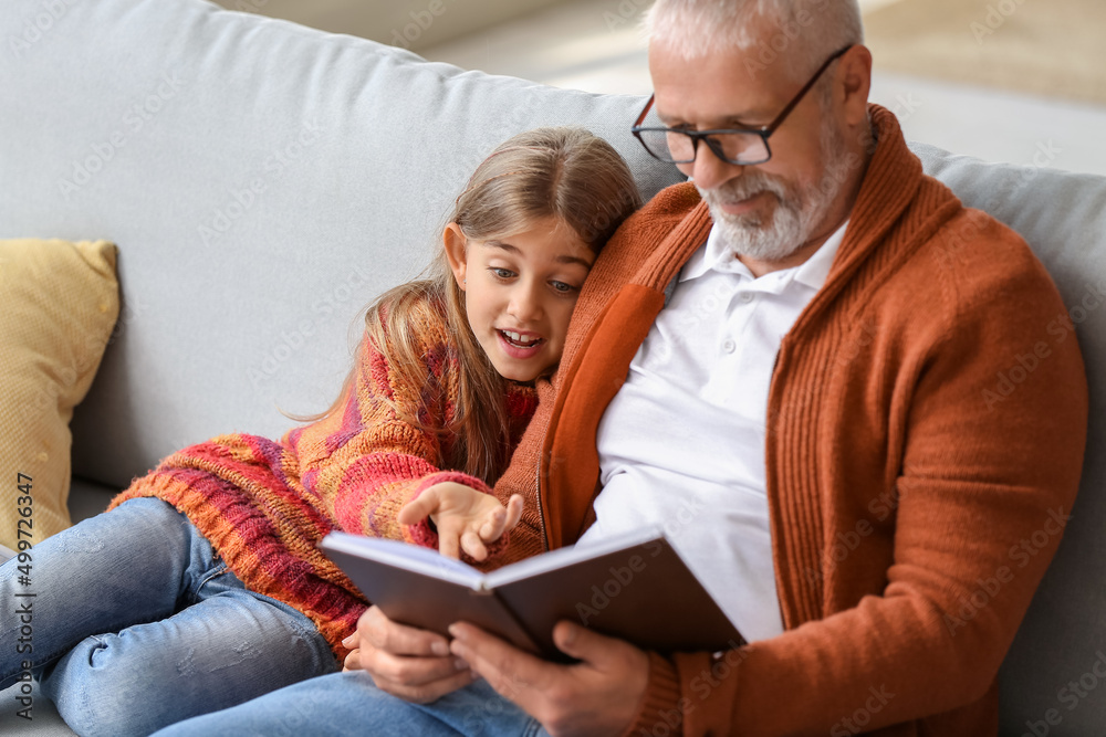 Little girl with her grandfather reading book at home