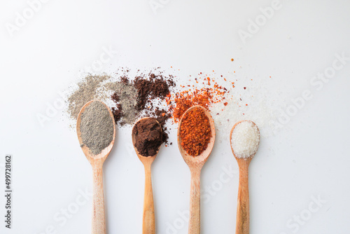 Various spices on wooden spoons on white background
