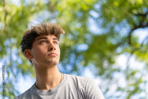 Confident young blonde man portrait, summer trees background. Copy space