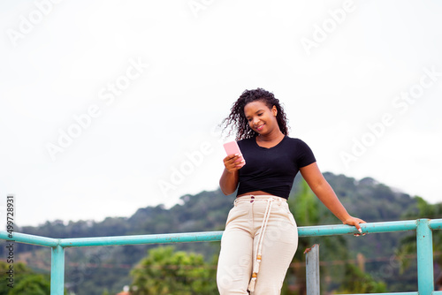 Young happy black woman holding a smartphone. Using mobile app or social networks on smartphone on the street.