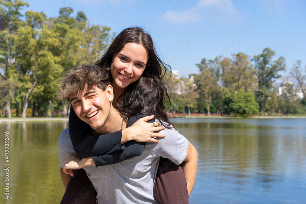 Young couple at a lake. Boyfriend carrying his girlfriend on piggyback. Funny and happy expression Young couple at a lake. Boyfriend carrying his girlfriend on piggyback. Funny and happy expression