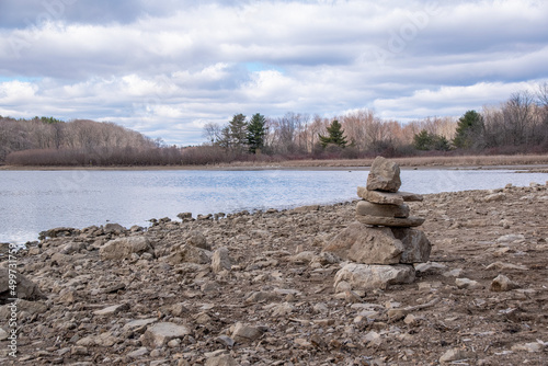 An inukshuk stands on the shore of Christie Lake near Crooks Hollow in Hamilton, Ontario under a cloudy sky.