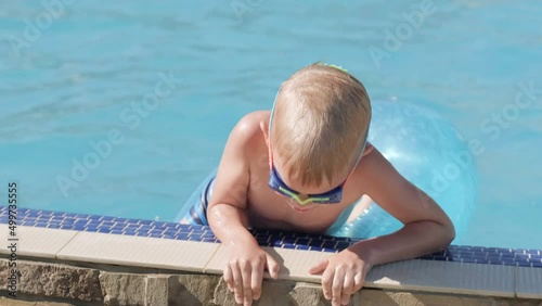 Little boy in swimming pool, child having fun, sitting on blue swimming ring, playing under water. Summer travel family hotel vacation tourists photo