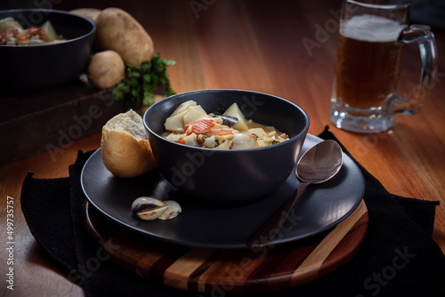 Seafood Soup in a black plate on wooden surface with a glass of beer