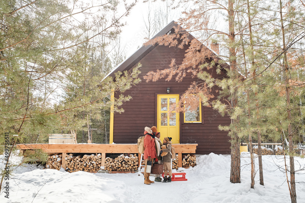 Naklejka premium Contemporary family of parents and little son in winterwear standing by their country house located in deep woods among pinetrees