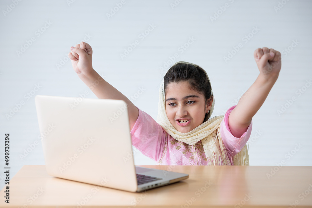 muslim girl using a laptop computer and raised hand for celebrating good news on the table