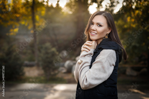 Portrait of a cute young woman among the autumn foliage in the park in a sweater and a warm vest