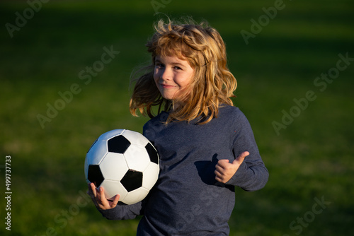 Boy holding soccer ball, close up sporty kids portrait. Young soccer player show thumbs up success sign. © Volodymyr