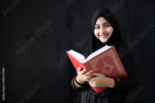 Fotografie, Obraz muslim girl reading a holy book quran on black background