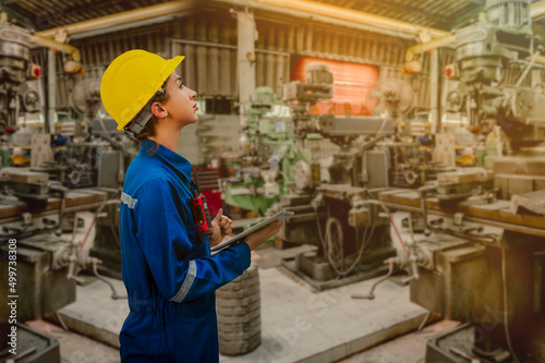 Portrait of Engineering female hardworking with helmet on head in vest and with tablet in hands posing in factory