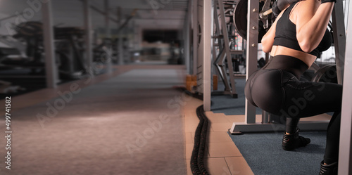 Attractive young athletic woman is exercising in the gym. close-up muscular woman squatting with a barbell back view without a face. Banner. © mtrlin