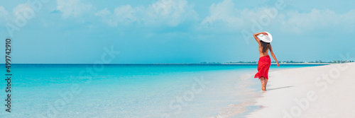 Beach vacation woman walking on summer travel Caribbean holiday wearing white sun hat and sarong skirt. Ocean panoramic banner background. Elegant lady tourist