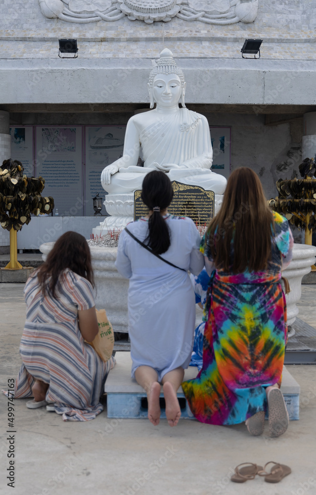 three dark-haired women kneeling in pray in front of a statue of Buddha