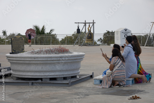 Photography three dark-haired women kneeling in pray in front of a statue of Buddha