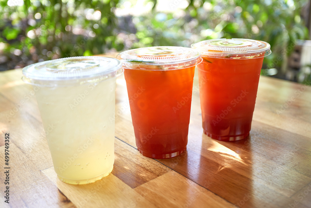 Iced lemon tea and honey lemon soda in plastic cups with lids placed on wooden tables, Thai herbal drinks.