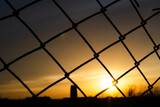 Cobwebs on a metal fence in rhombuses. Blurred Sunset Background