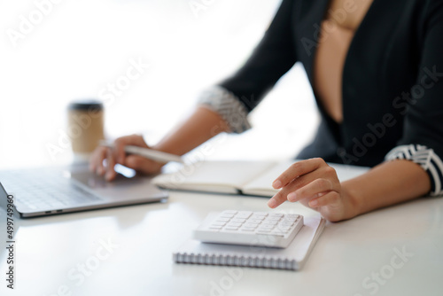 Business woman using a calculator to check income and budget and analyzing graphs in office.